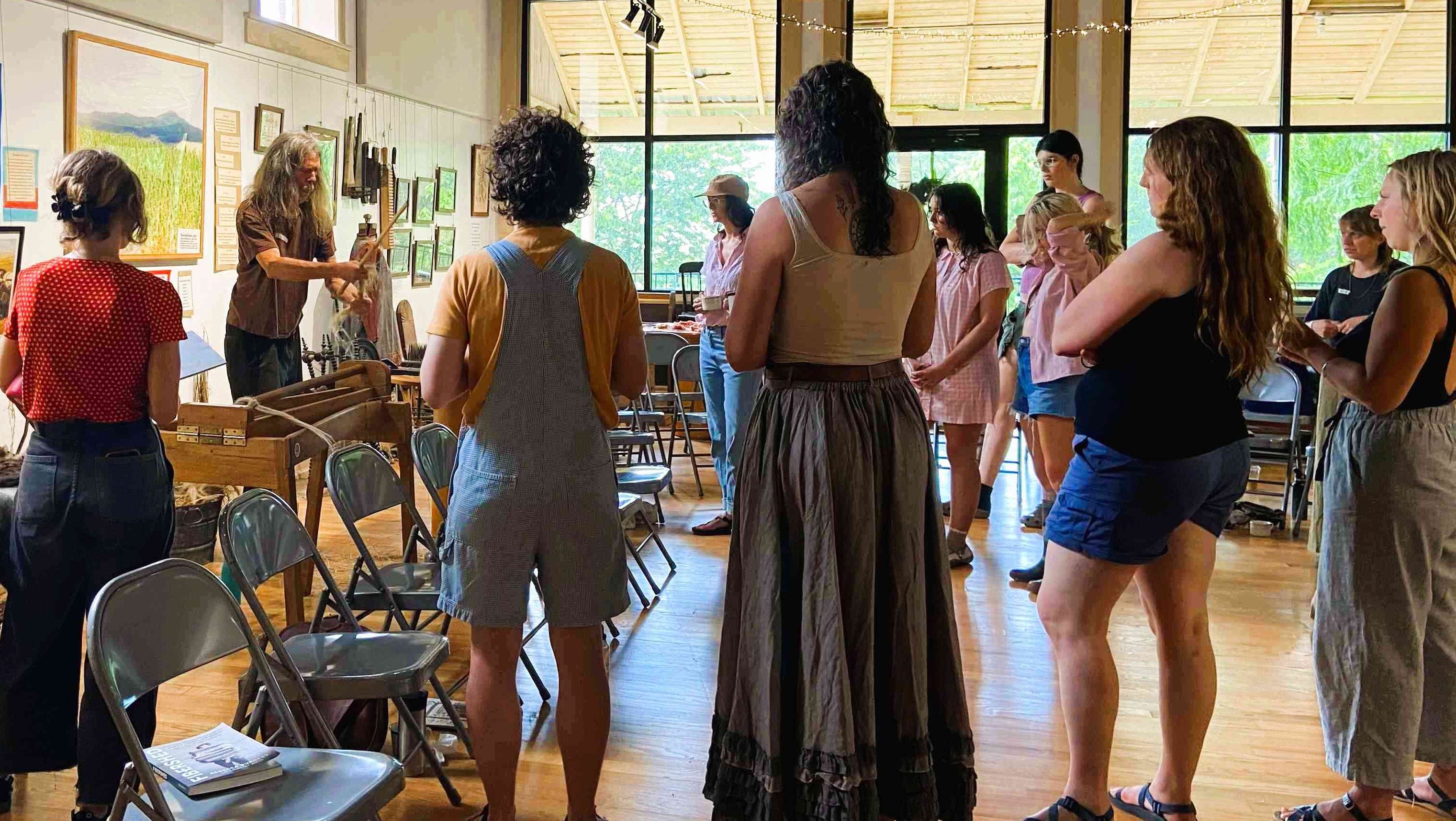 A group of people stand around a man demonstrating how to process flax fibers.